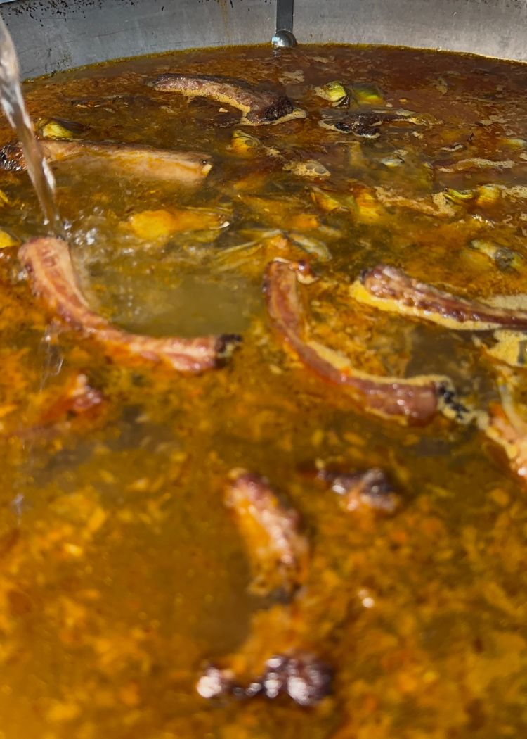 Verter agua caliente en paella de costillas y alcachofas