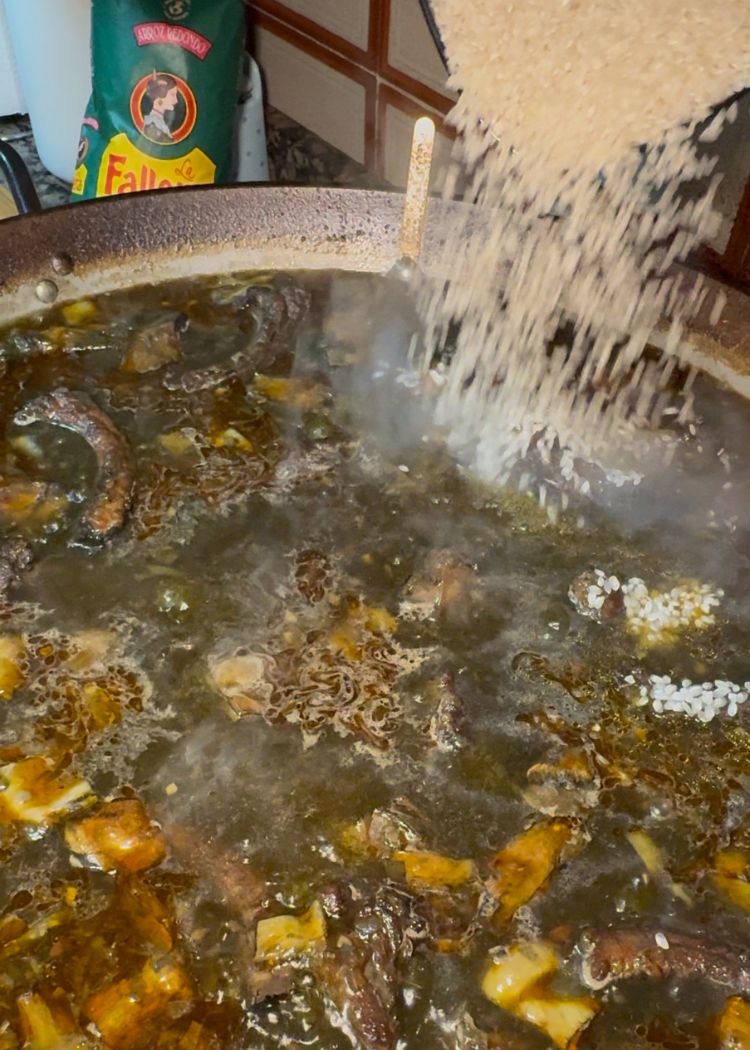 Echar arroz en paella de costillas y alcachofas